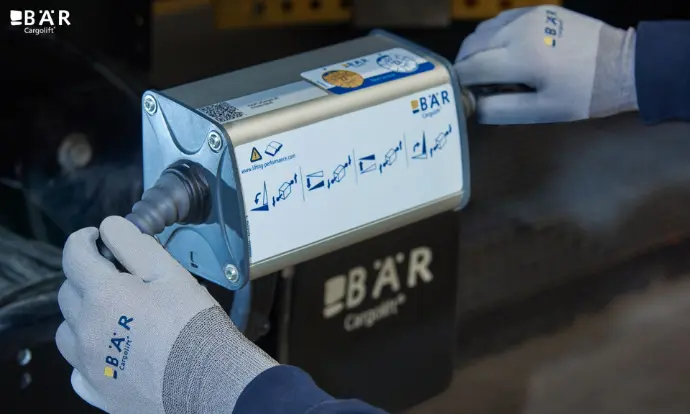 Zwei Hände in Handschuhen bedienen die Hebebühne mit dem Bär Bedienkasten