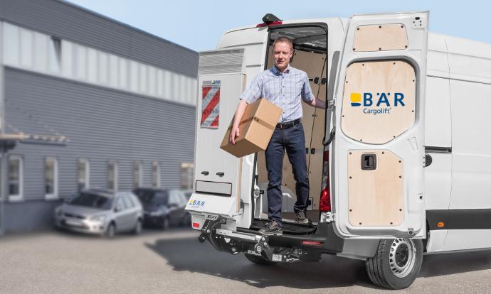 Fahrer steigt mit Paket in der Hand aus dem Van, vorbei an der unbewegten BÄR Ladebordwand