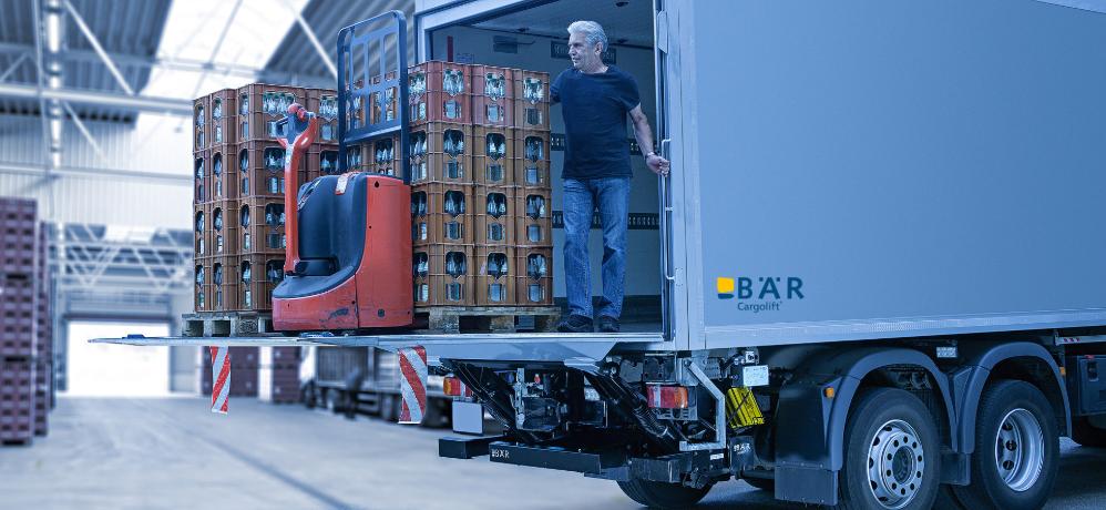 Lkw-Fahrer entlädt Getränkeliste und einen Elektrohubwagen mit einer BÄR Ladebordwand in einer Halle